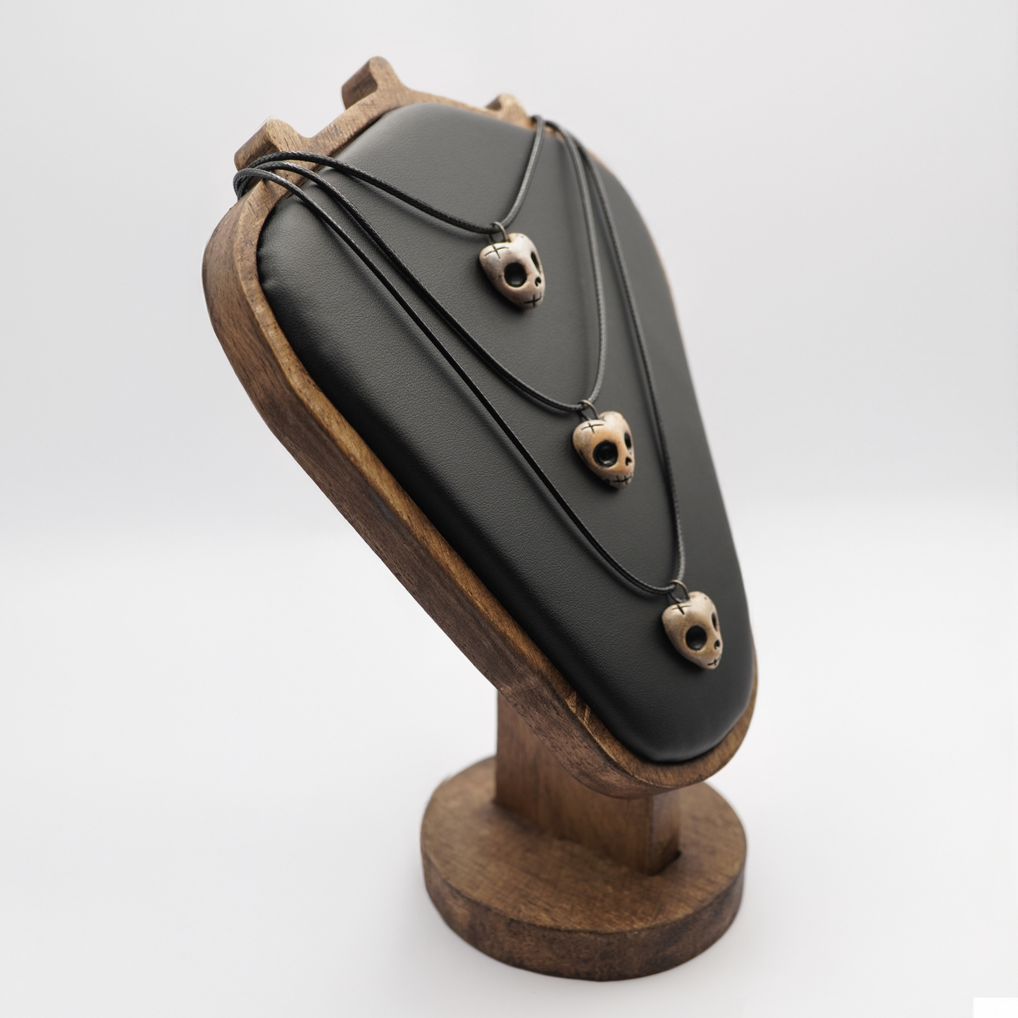 Black necklace with skull pendants on a wooden stand against a white background