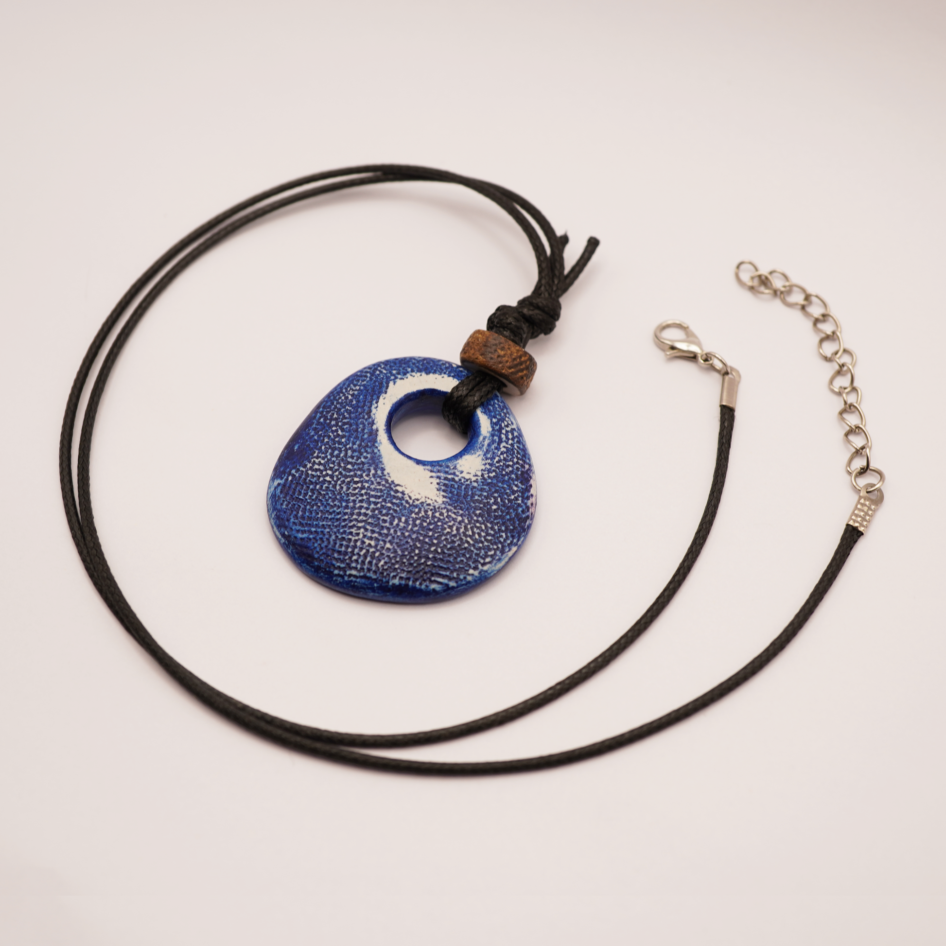 Necklace with a blue pendant and black cord on a light gray background