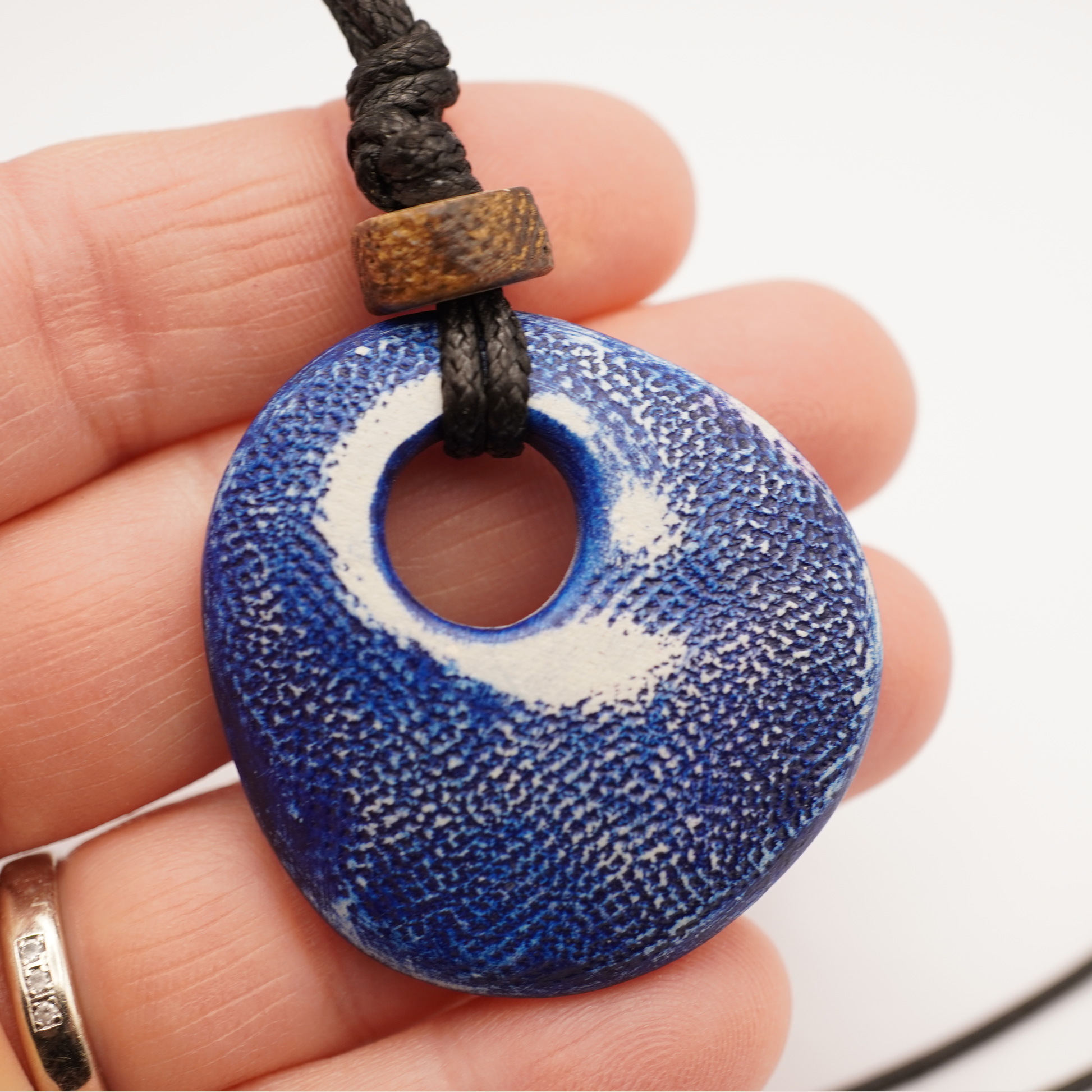 Blue textured pendant on a cord held between fingers with a white background