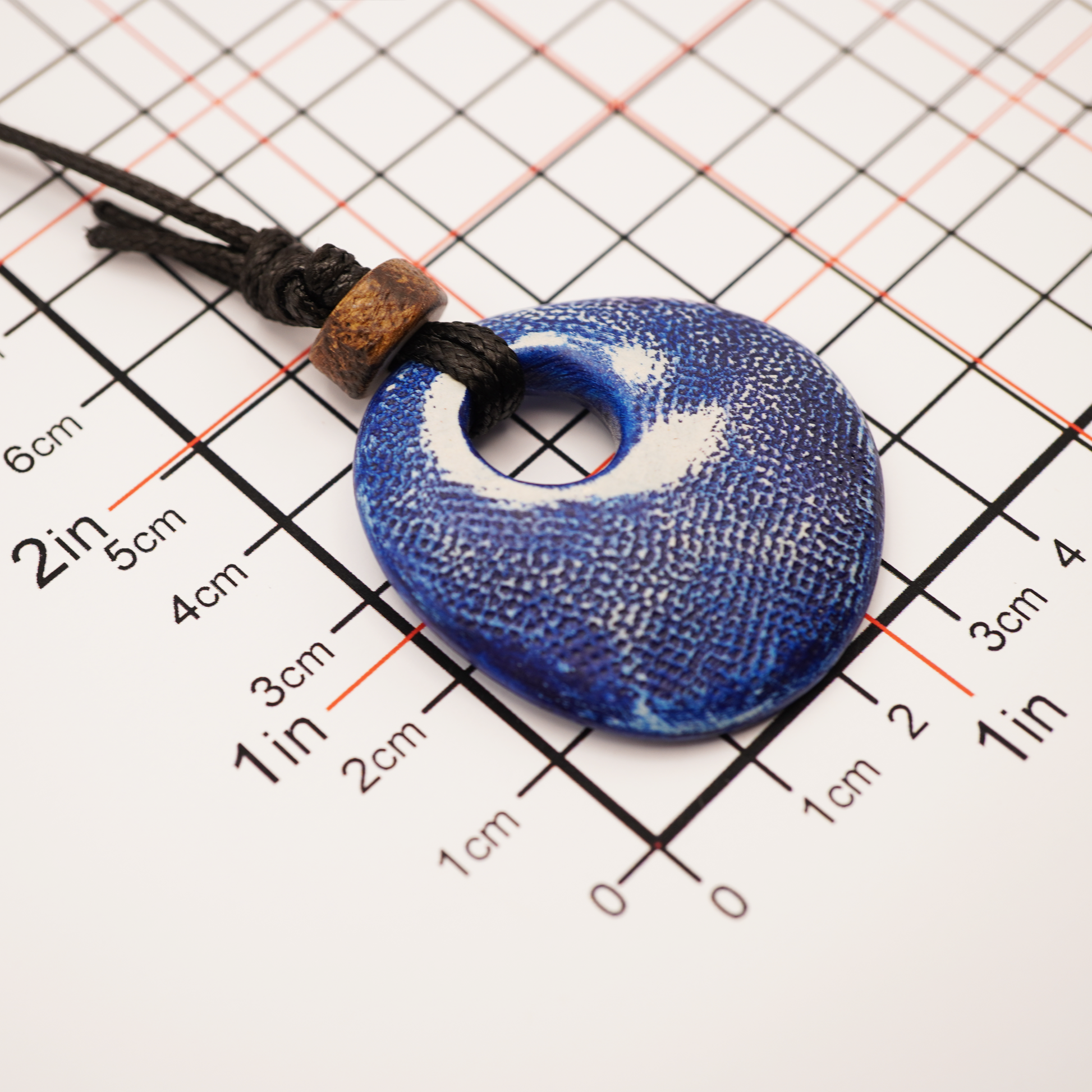 Blue pendant necklace on a grid background with measurements