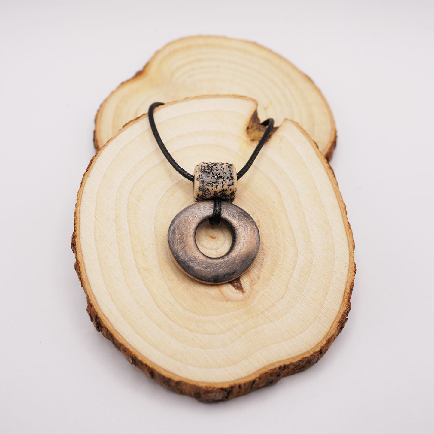 Handmade ceramic ring pendant with a textured square bead displayed on natural wooden slices.