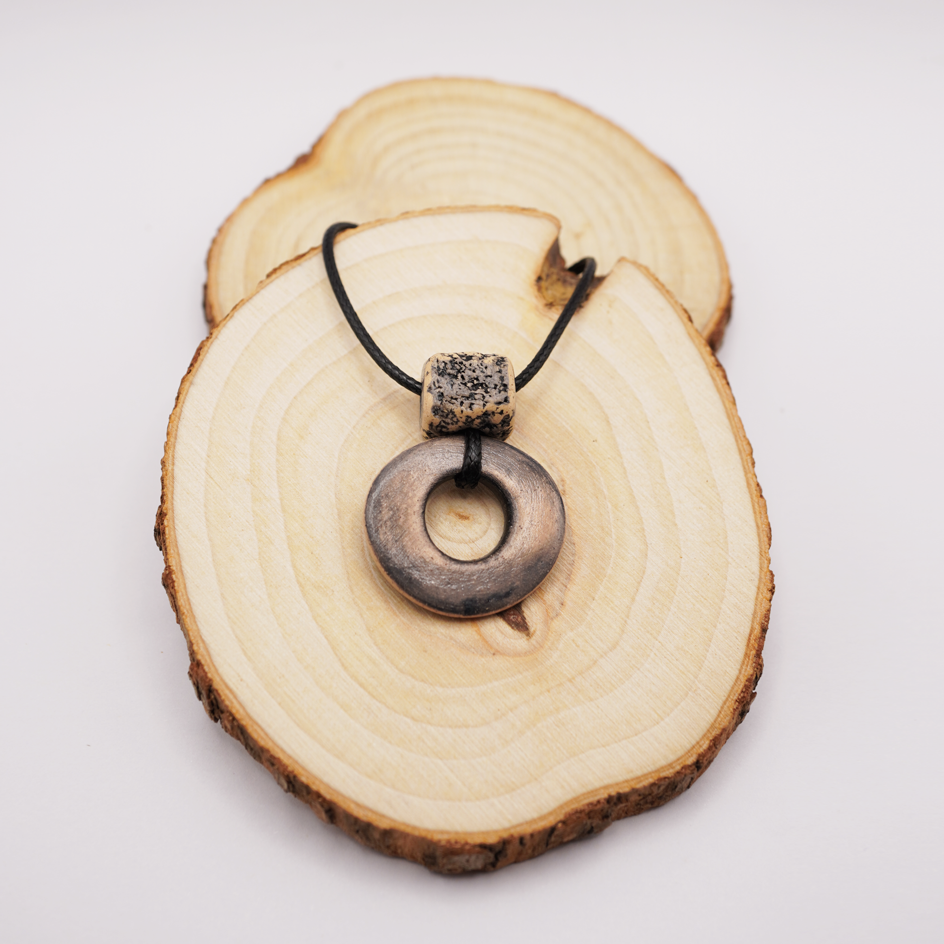 Handmade ceramic ring pendant with a textured square bead displayed on natural wooden slices.