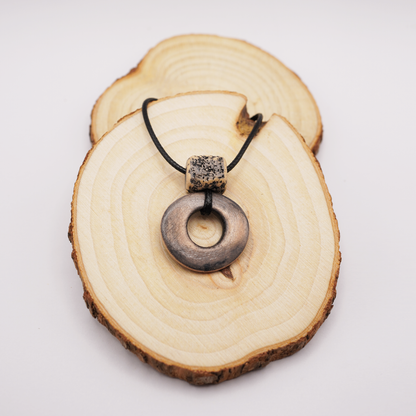 Handmade ceramic ring pendant with a textured square bead displayed on natural wooden slices.