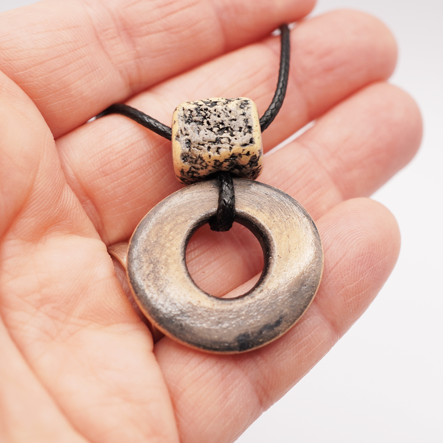Handmade ceramic ring pendant with a textured square bead held in a hand.