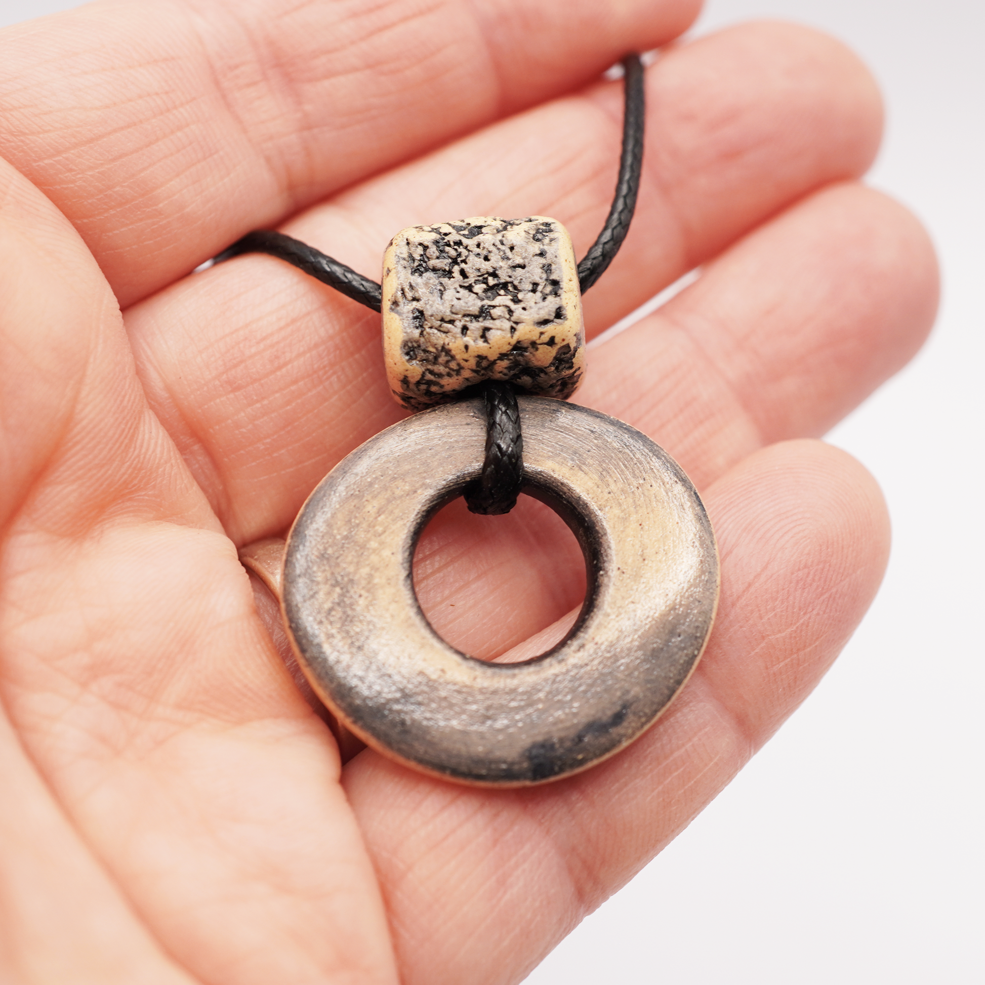 Handmade ceramic ring pendant with a textured square bead held in a hand.