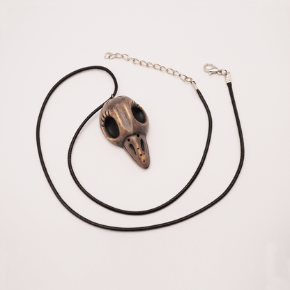 Handmade ceramic raven skull necklace on black cord, displayed on light background.