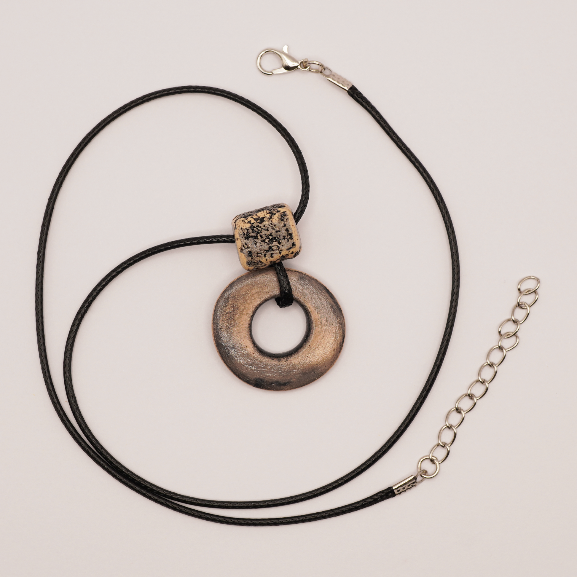 Handmade ceramic ring pendant with textured bead on a black cord, displayed on a light background.