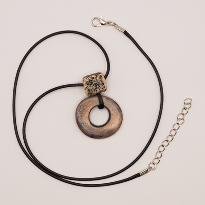 Handmade ceramic ring pendant with textured bead on a black cord, displayed on a light background.