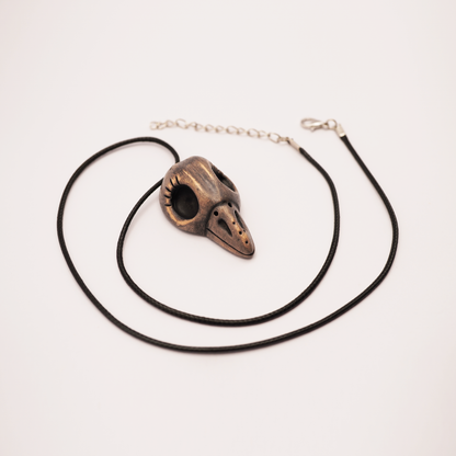 Handmade ceramic raven skull pendant on black cord against white background.