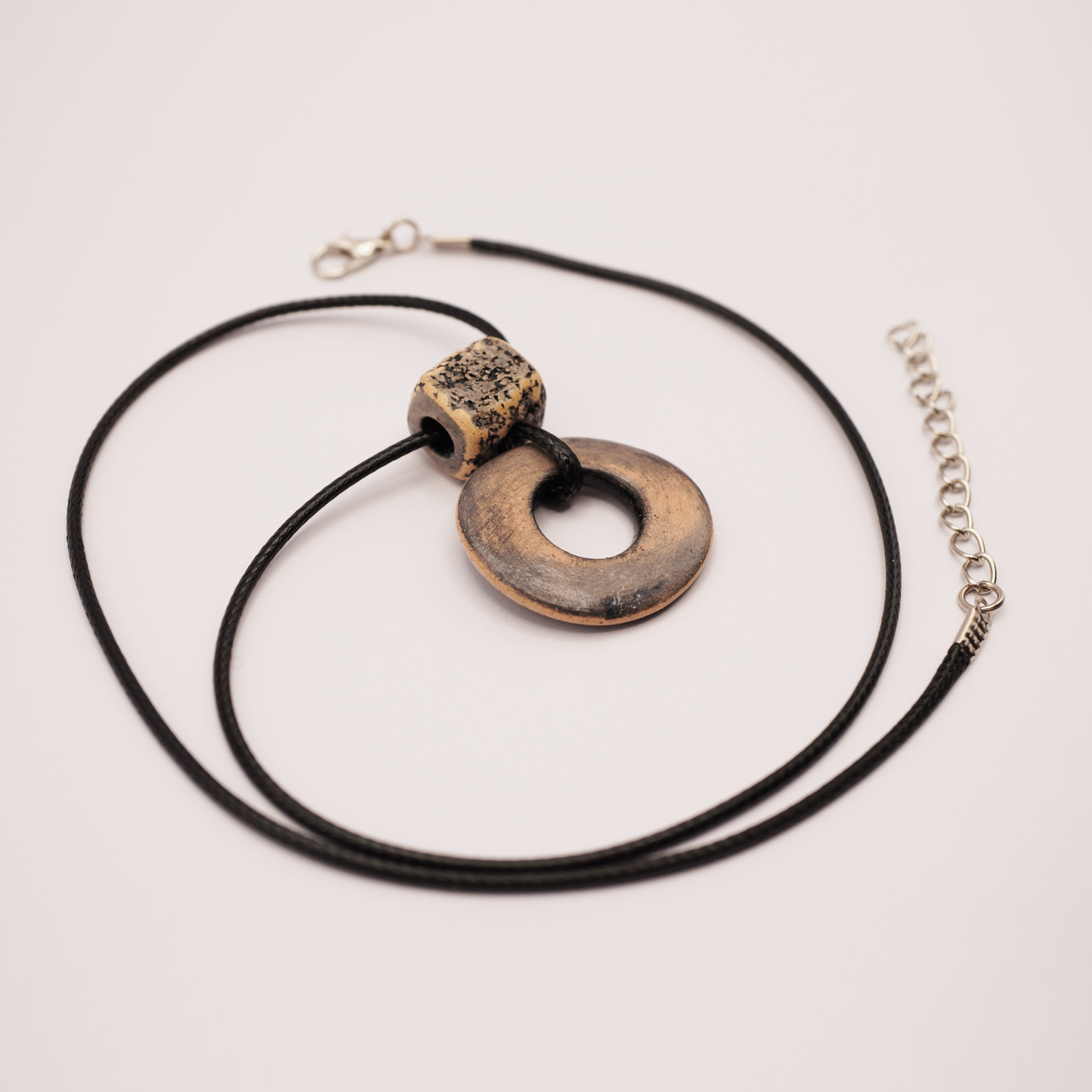 Handmade ceramic ring pendant on a black cord displayed on a light background.