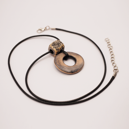 Handmade ceramic ring pendant on a black cord displayed on a light background.