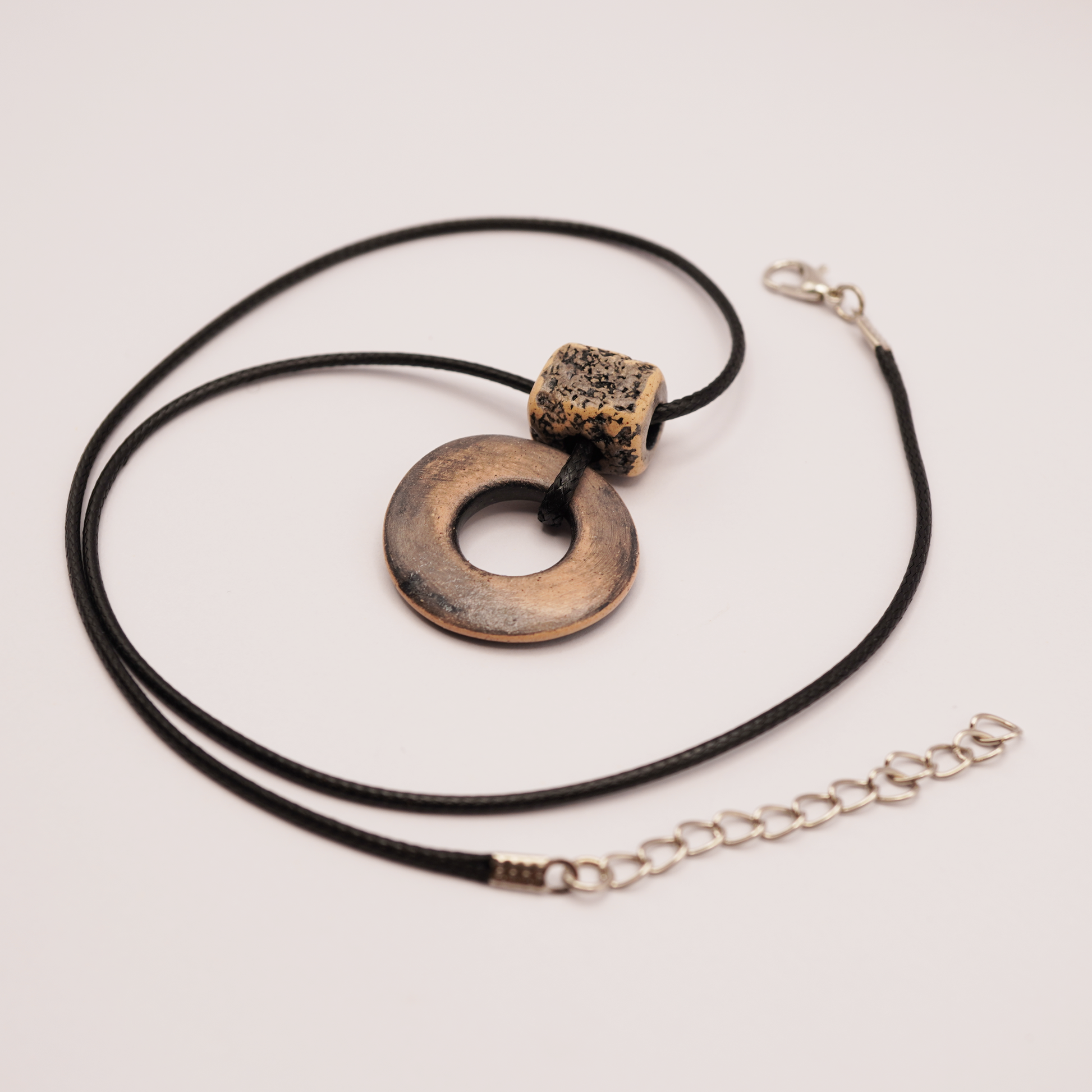Handmade ceramic ring pendant on a black cord displayed on a soft light background.