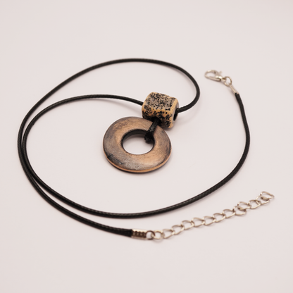 Handmade ceramic ring pendant on a black cord displayed on a soft light background.