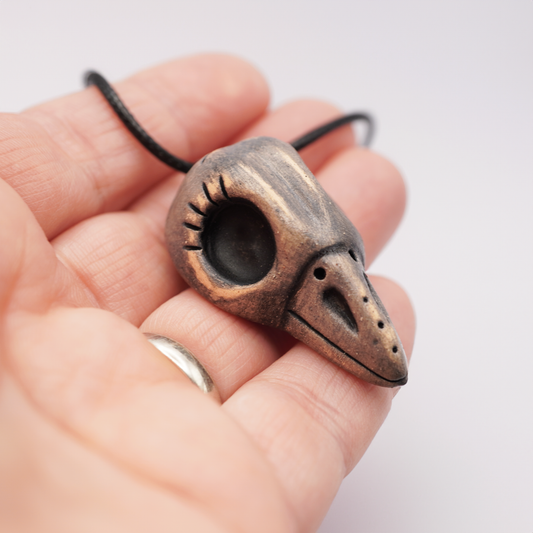 Handmade ceramic raven skull pendant in a hand on a light background.