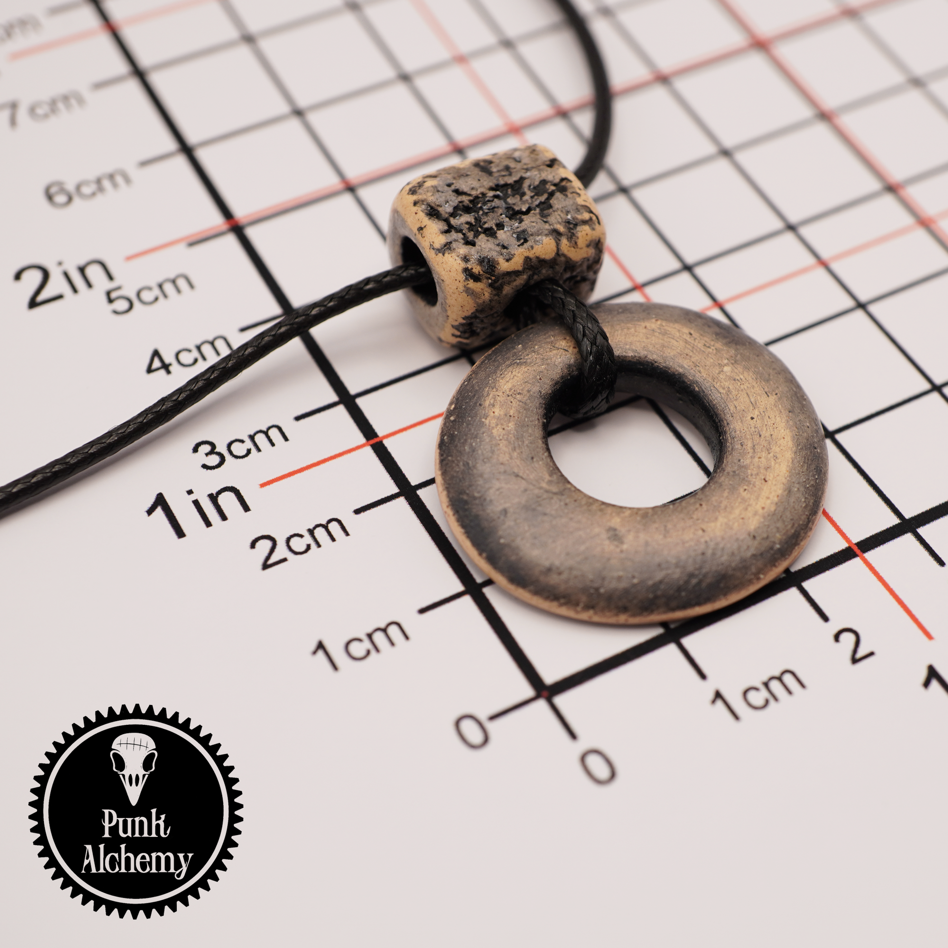 Handmade ceramic ring pendant with a textured square bead shown on a measurement grid with Punk Alchemy logo.