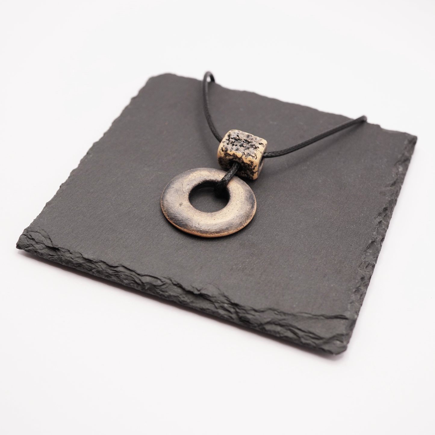 Handmade ceramic ring pendant with a textured square bead displayed on a dark slate tile.
