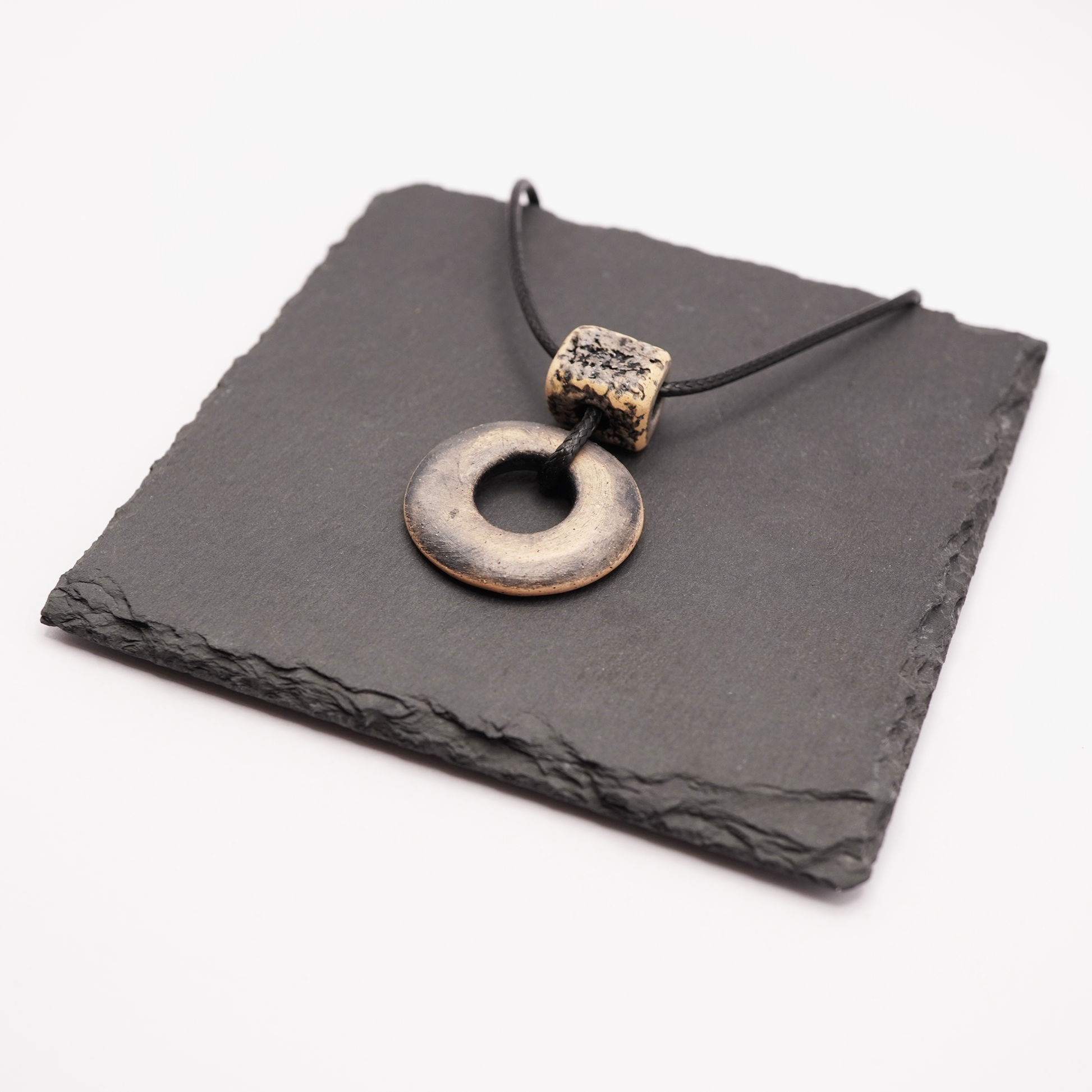 Handmade ceramic ring pendant with a textured square bead displayed on a dark slate tile.