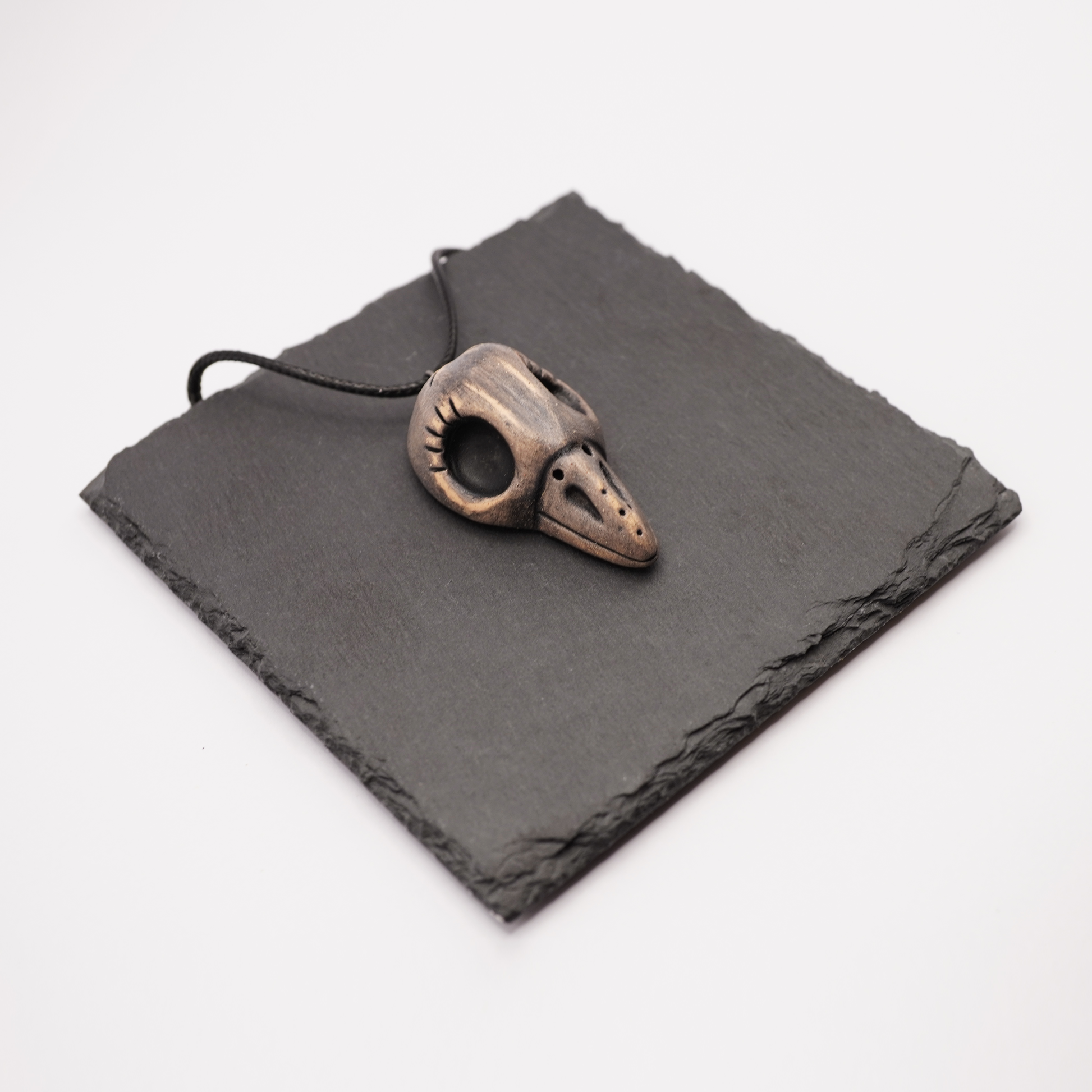 Ceramic bird skull necklace placed on a dark slate display.