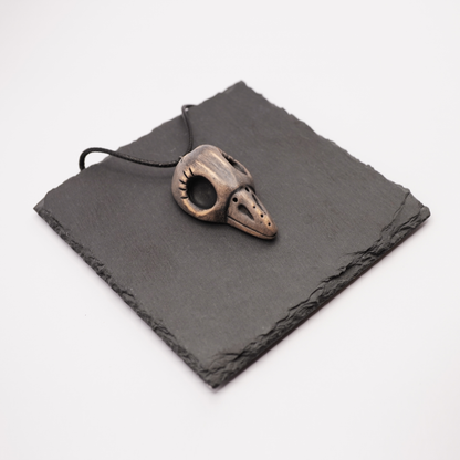 Ceramic bird skull necklace placed on a dark slate display.