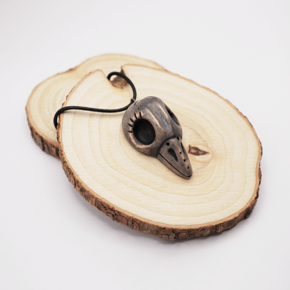 Handmade ceramic raven skull pendant displayed on natural wooden slices.