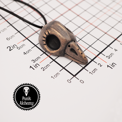 Handmade ceramic raven skull pendant on a measurement grid showing size in inches and centimeters.