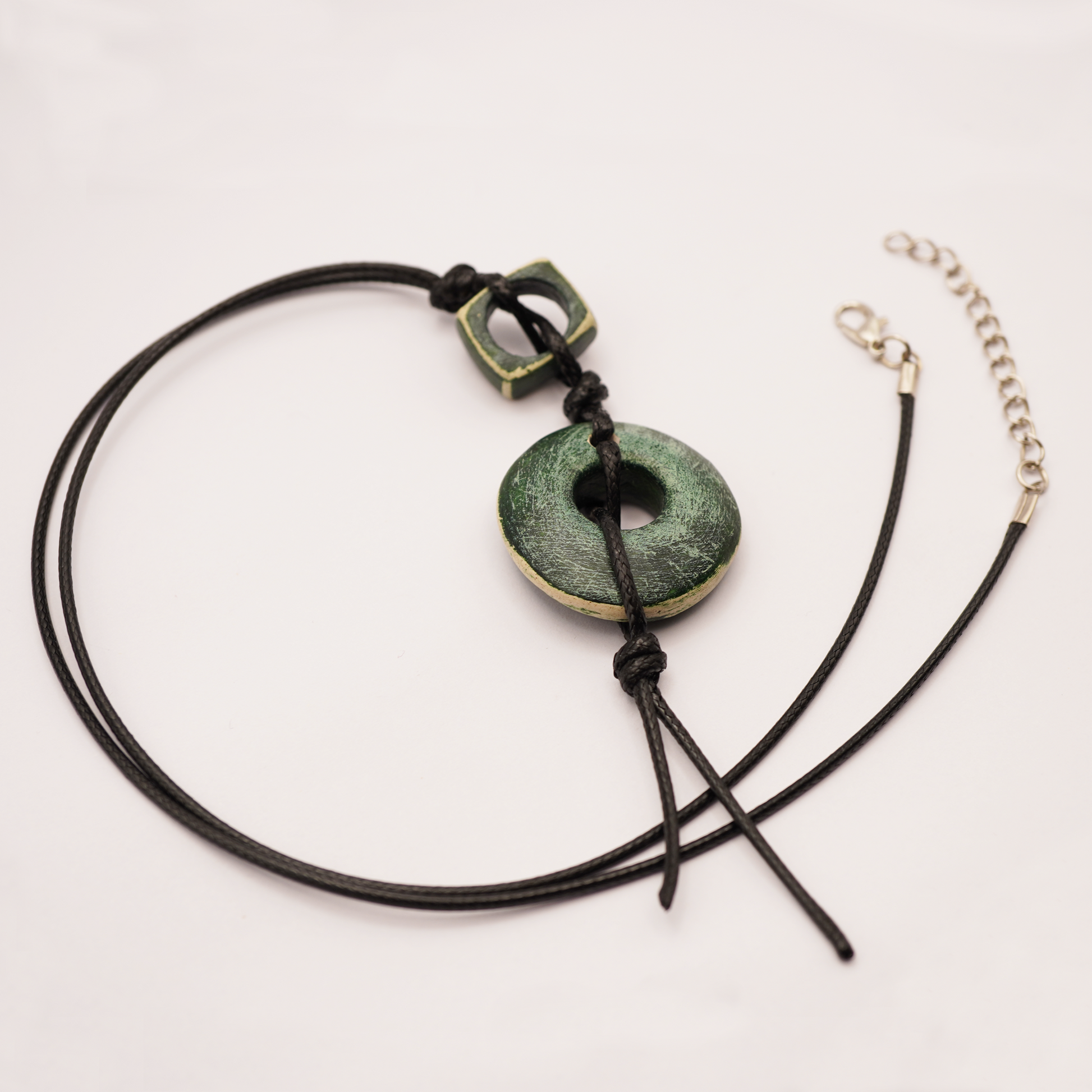 Necklace with green pendant and black cord on a light background