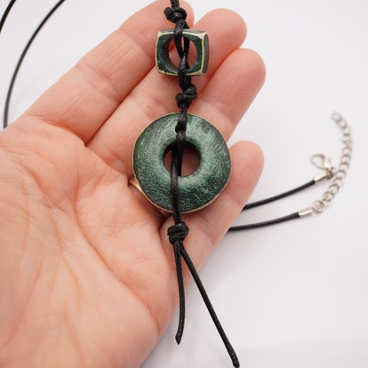 Hand holding a green pendant necklace with a white background