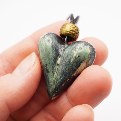 Heart-shaped green stone pendant held in a hand with a white background
