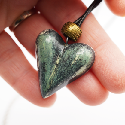 Heart-shaped stone pendant on a cord held in a hand against a white background